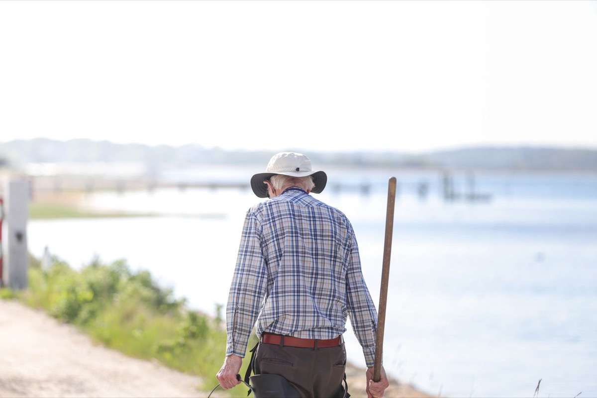 水辺の道を歩く年配の男性の後ろ姿