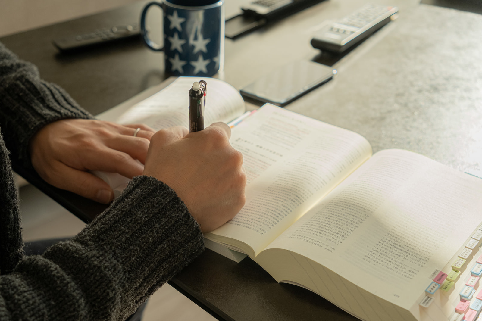 机の上で教科書を開き、ペンを持って勉強する手元
